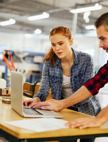 Young man and young woman using a laptop while working in a printing press office